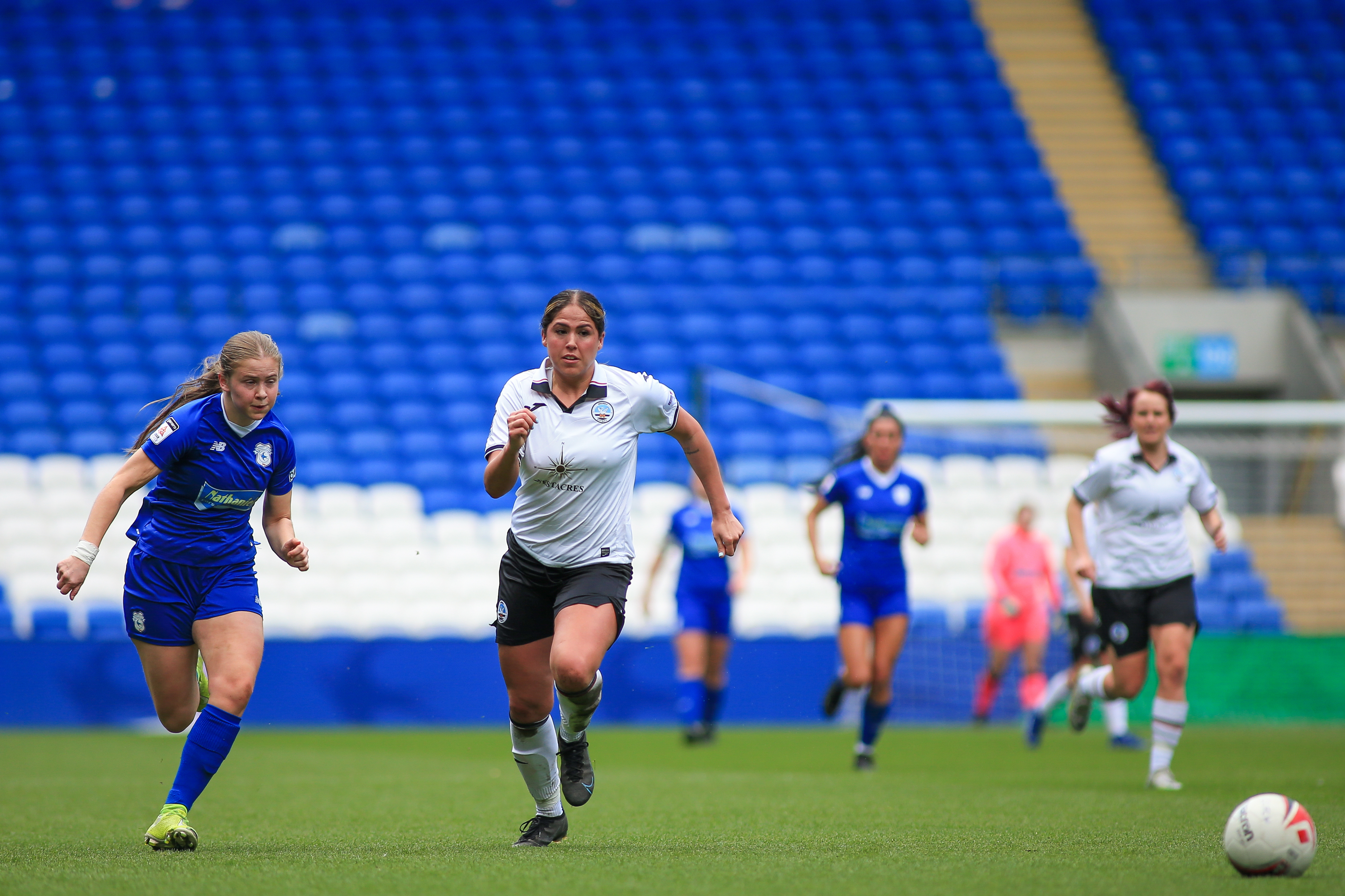 A Cardiff City and a Swansea City player chase an Adran Premier foot ball.