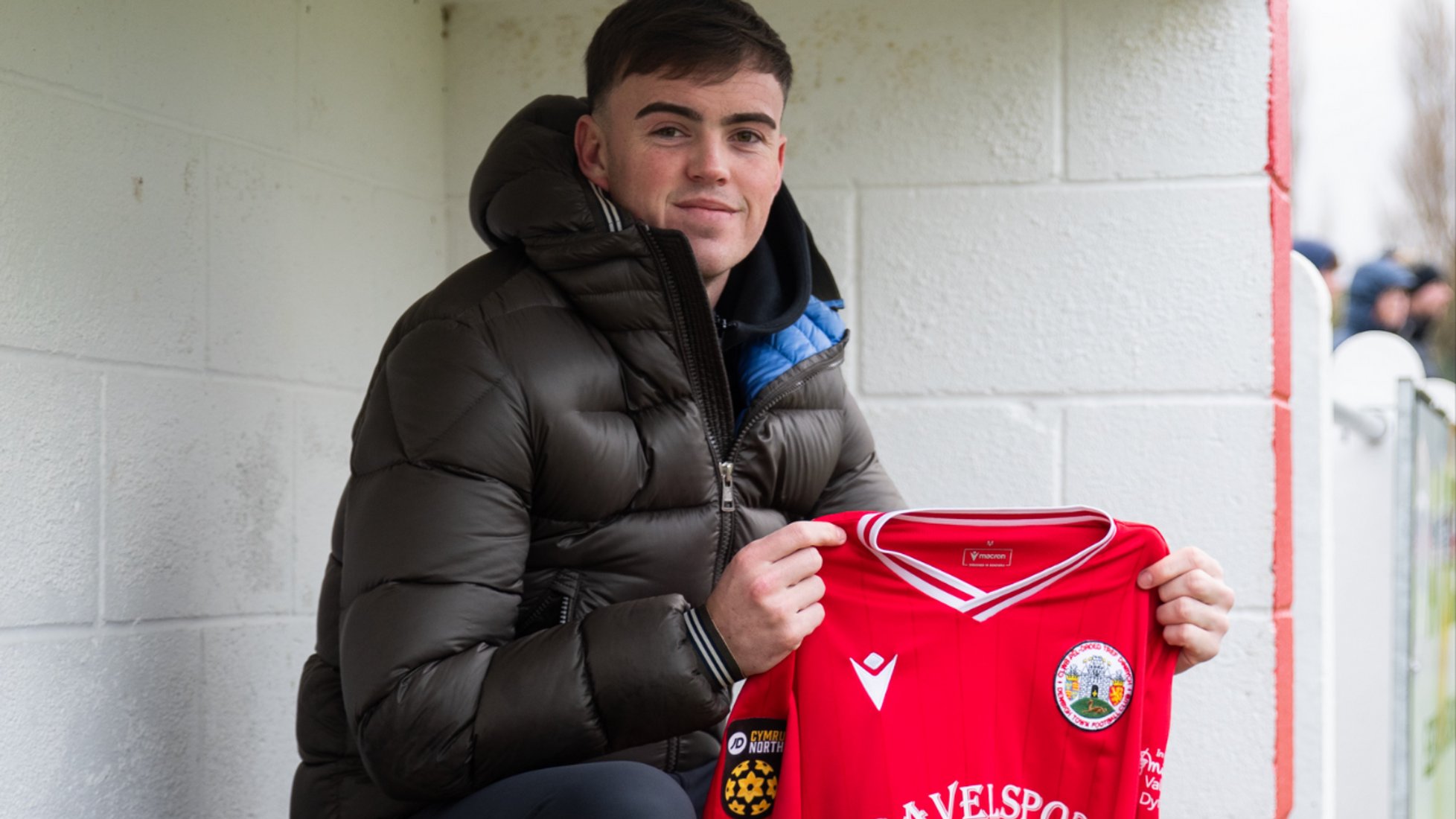 Kyle Cooper poses with a Denbgh Town shirt sat in the dugout at Central Park, the home of the Cymru Leagues North club.