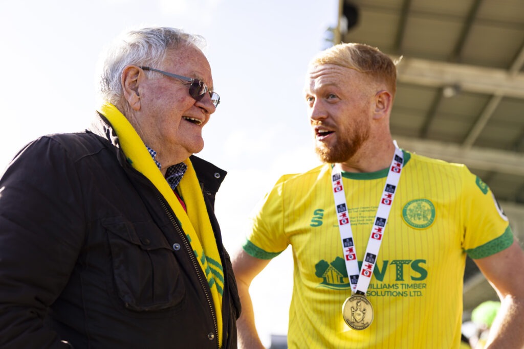 NEWPORT, WALES - 12 APRIL 2026: Dafydd Iwan with Caernarfon Town's Sion Bradley during 2025/26 JD FAW Welsh Cup Final fixture between Caernarfon Town F.C & Flint Town United F.C at Rodney Parade, Newport, Wales.
