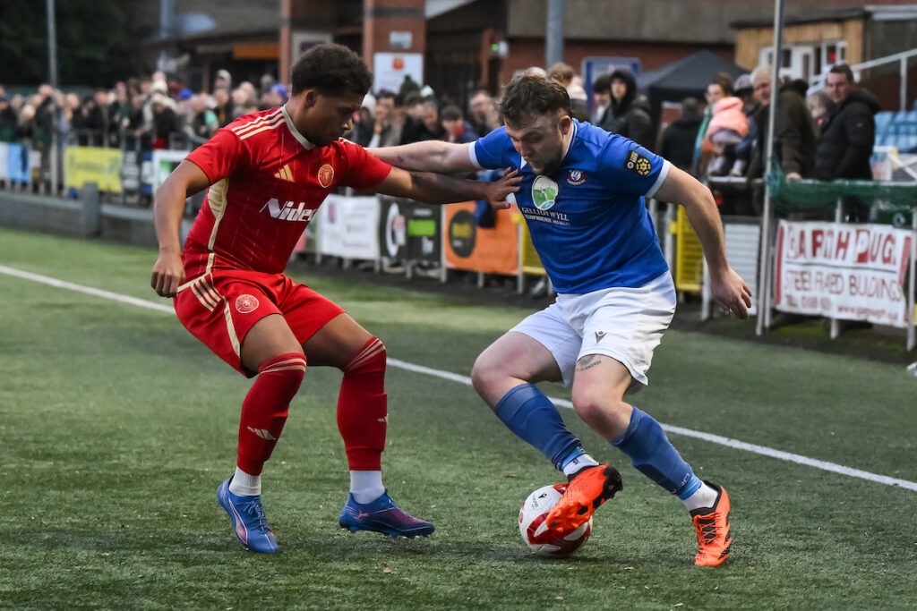 Max McLaughlin of Caersws and Cuba Cline of Newtown battles for the ball during the Welsh Blood Service League Cup North game between Newtown and Caersws at Latham Park in Newtown