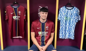 Cardiff Met and Bristol City defender Jack Hooper poses next to the 2026/27 Cymru Premier shirts