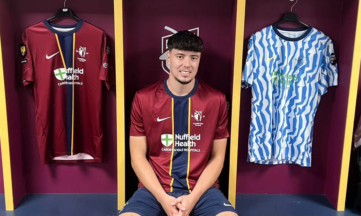 Cardiff Met and Bristol City defender Jack Hooper poses next to the 2026/27 Cymru Premier shirts